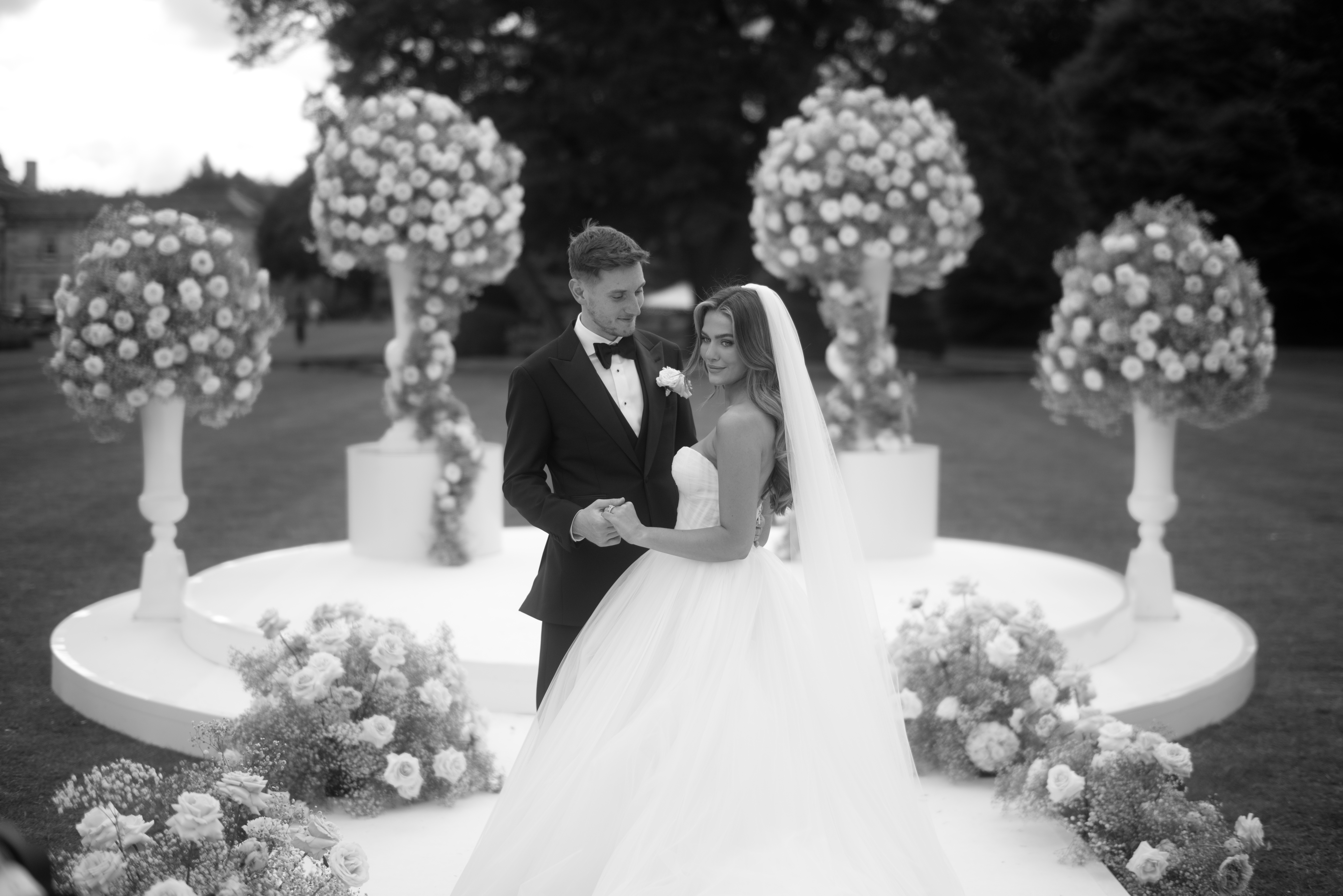 David Brooks and Flora share a joyful moment during their wedding ceremony at Grantley Hall, with elegant floral arrangements in the background.