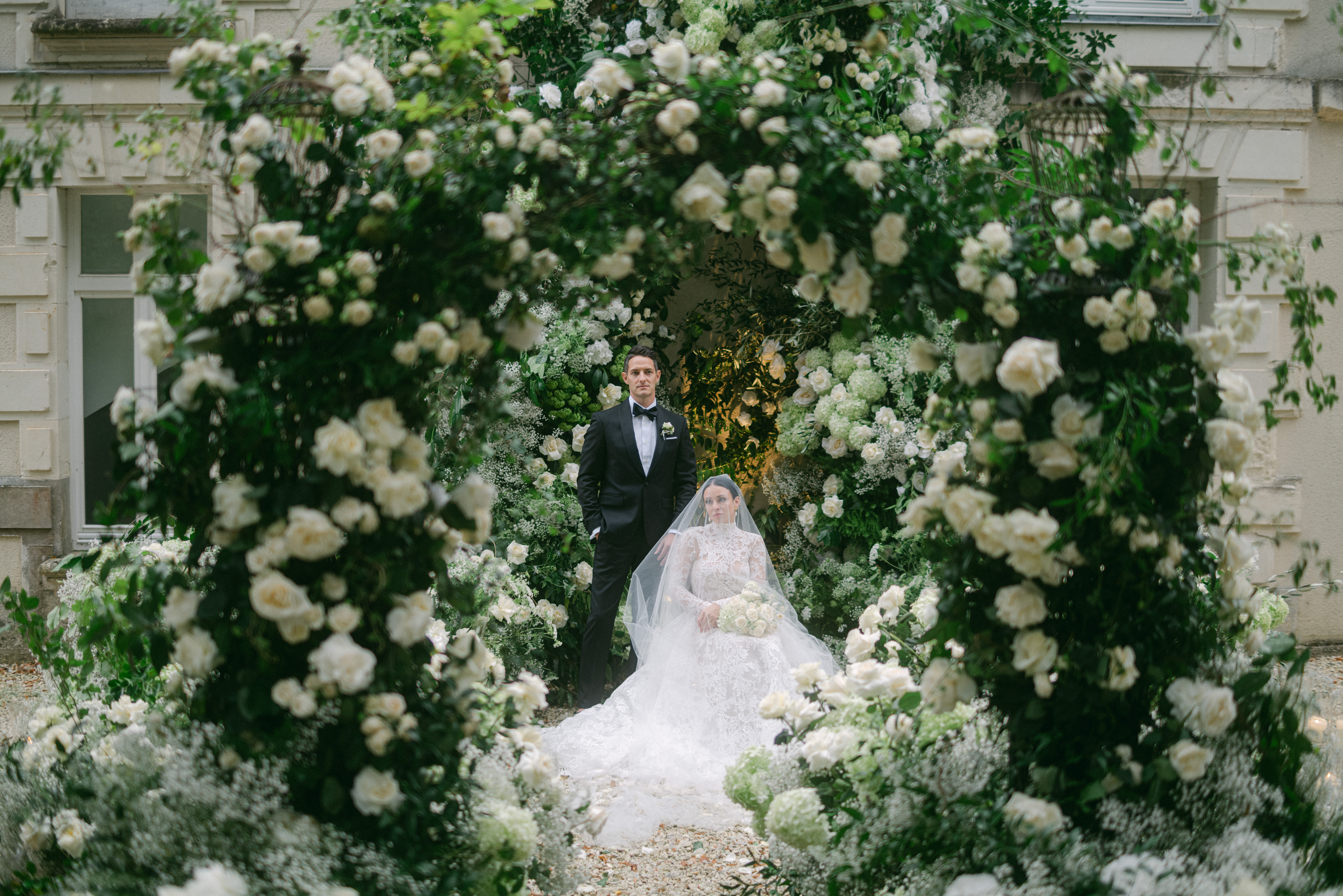 Michelle and Matt sharing a quiet moment beneath a floral arch in the French countryside, surrounded by soft candlelight and lush garden blooms.